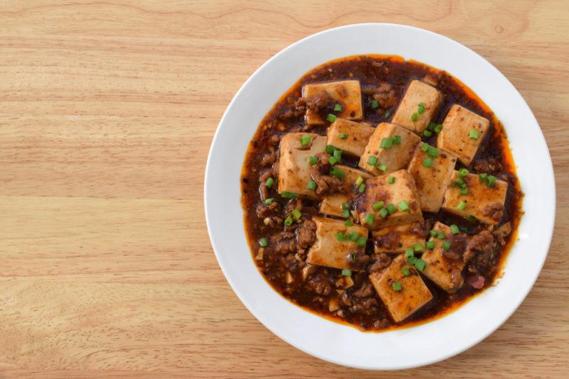 A white bowl on a light wooden table that contains ma po tofu