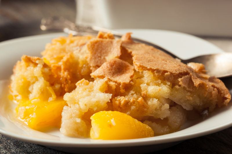 A white dish of peach cobbler with a spoon