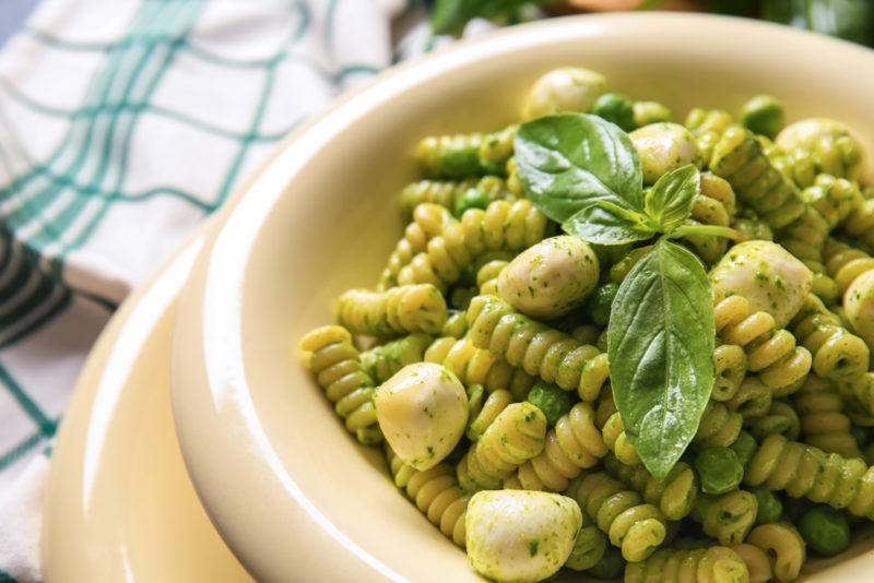 A light colored dish with pesto pasta and cheese next to a tea towel