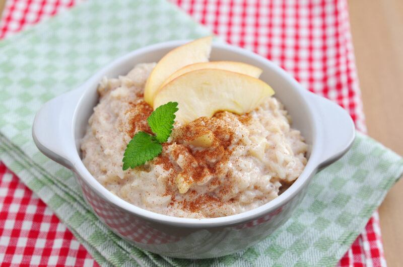 A white bowl that is filled with an apple, rice, and cinnamon dish