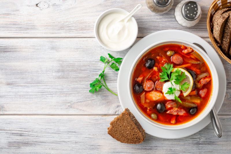 A wooden table with a white dish of solyanka soup