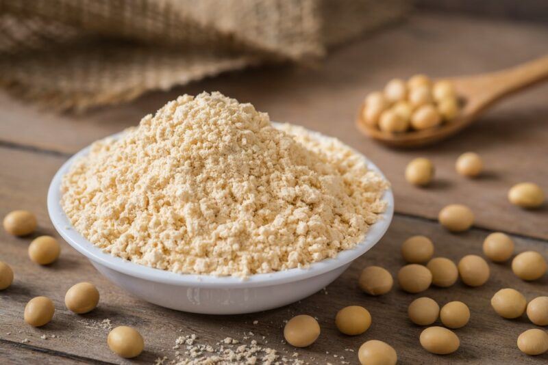 A white dish of soy powder on a table, with soybeans scattered around