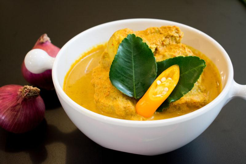 A white dish with handles that contains a Thai yellow curry and two leaves