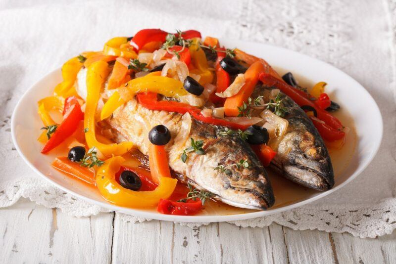 Two pieces of fish prepared in the escovitch style on a white plate covered with peppers