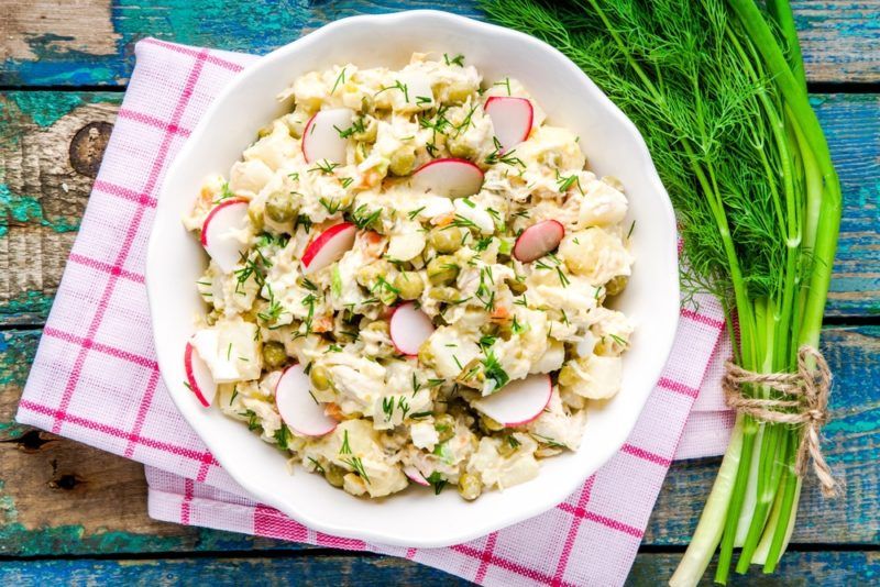 A white dish on a tea towel that contains a radish potato salad