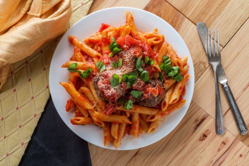 A white plate with a spicy pasta dish and a knife and fork