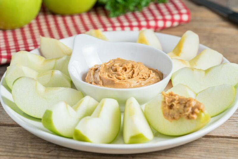 A white dish with apple slices surrounding a bowl of peanut butter dip