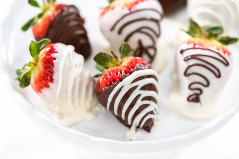 A white plate with chocolate dipped strawberries. Some are dipped in milk chocolate and others in white chocolate