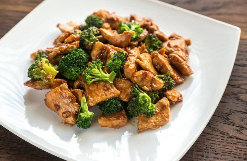 A white plate with a chicken and broccoli stir fry