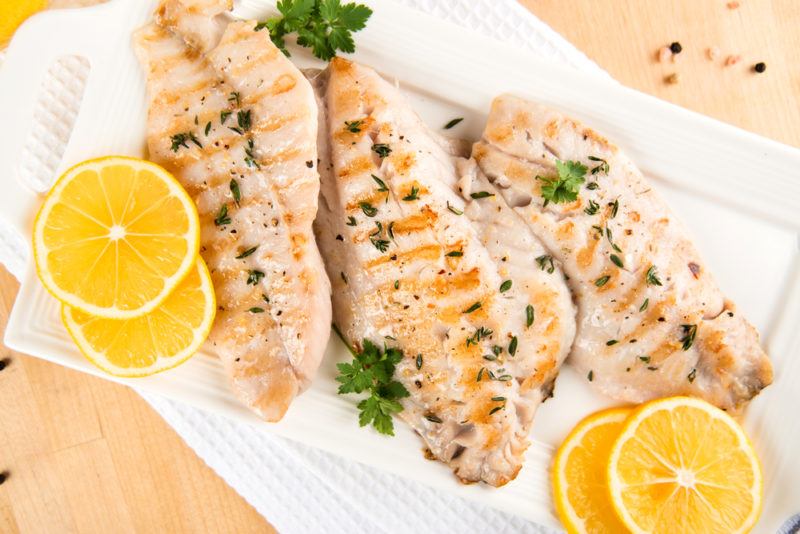 A white dish with grilled white fish and slices of lemons