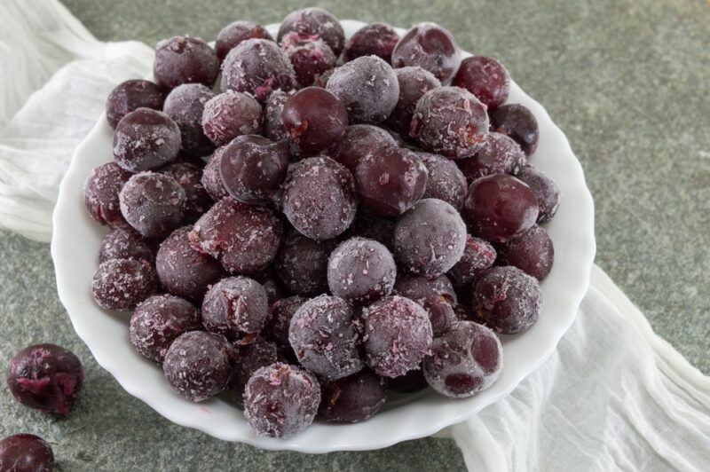 A white bowl containing frozen red grapes