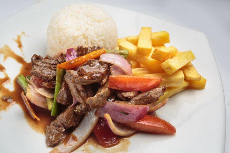 A white plate with stir fried beef, fries, and rice, which goes by the name lomo saltado