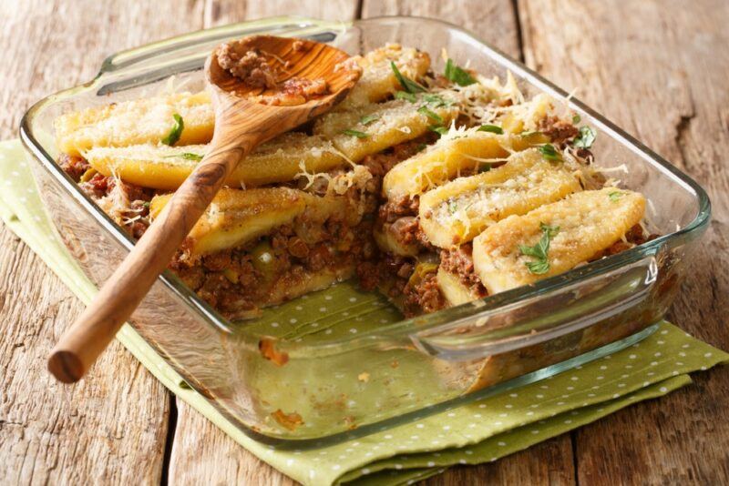 A square glass dish containing a meal called pastelon with a wooden spoon