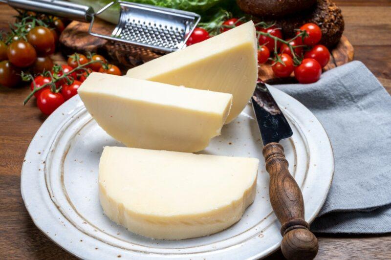 A white dish with wedges of provolone cheese, next to a knife