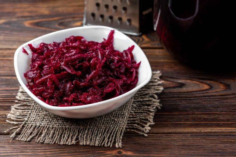 A white bowl with cooked shredded beets in front of a grater