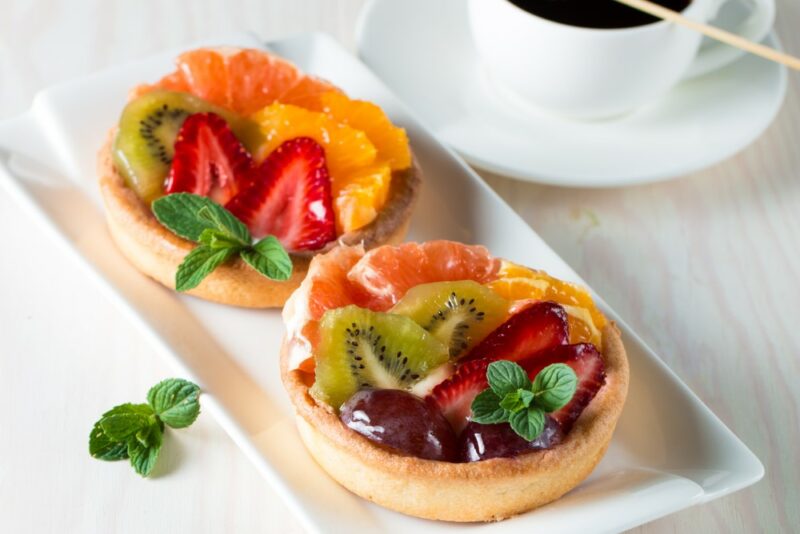 A rectangular white plate with two fruit tarts, each filled with many types of fresh fruit