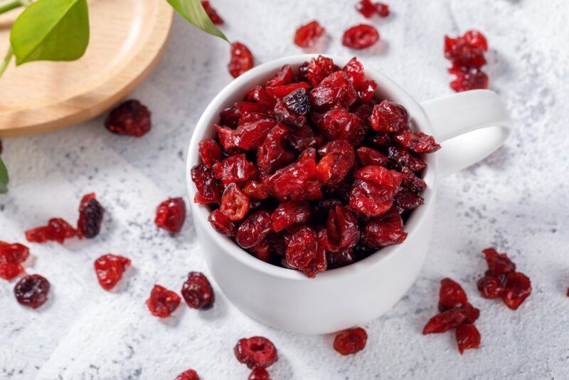 A white jug that is packed with dried cranberries. There are more dried cranberries scattered on the table. 