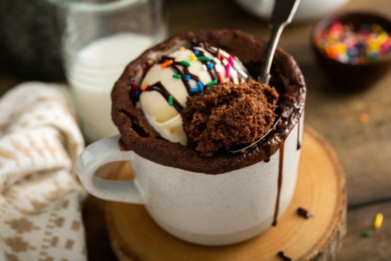 A white mug containing a chocolate mug cake and a spoon, topped with vanilla ice cream