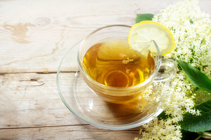 A glass mug and saucer, where the mug contains elderflower tea