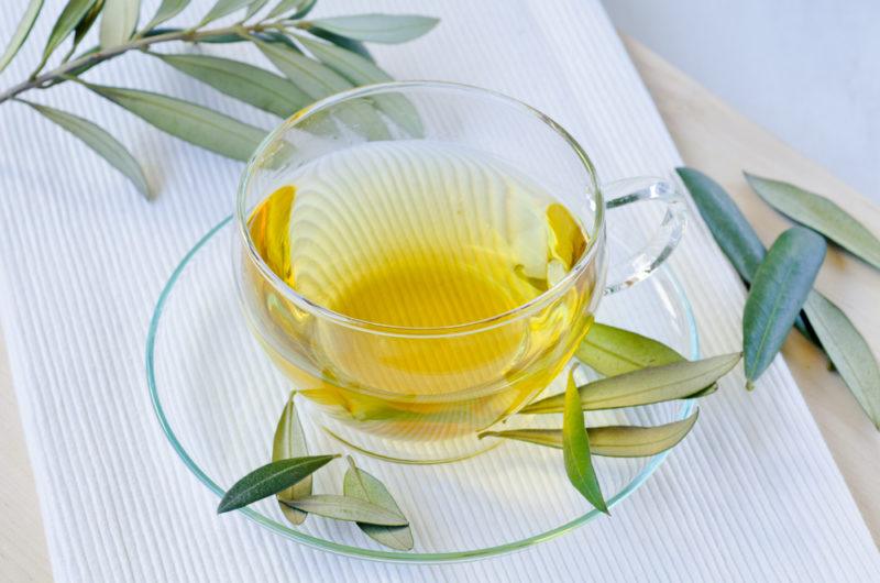 A glass mug and saucer with olive leaf tea, where there are olive leaves scattered around