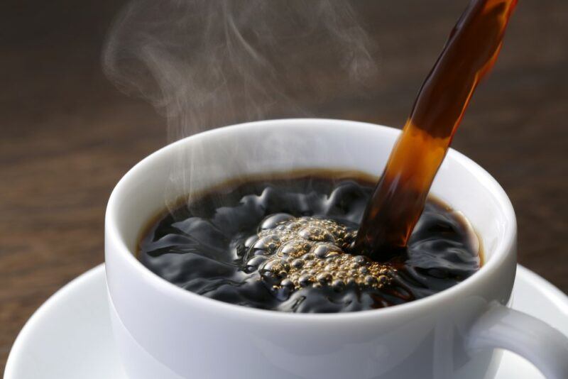 A white mug of coffee that's being poured