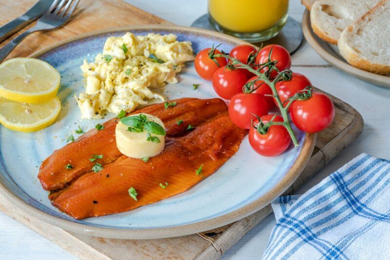 A light blue plate with kippers, scrambled eggs, and tomatoes