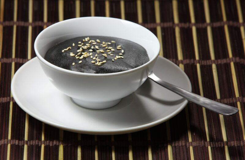 A slatted table or tray, with a white bowl and sauce, containing black sesame soup