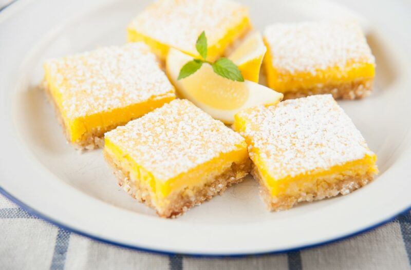 A white plate with square lemon bars that are topped with powdered sugar