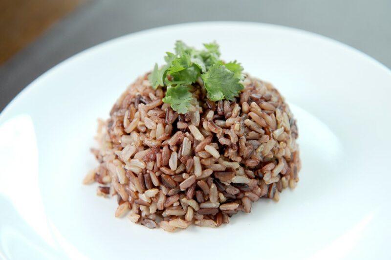 A white plate with a pile of brown rice and some green leaves on top