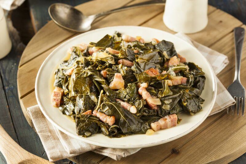 A white plate with cooked collard greens and some type of protein, being served outside