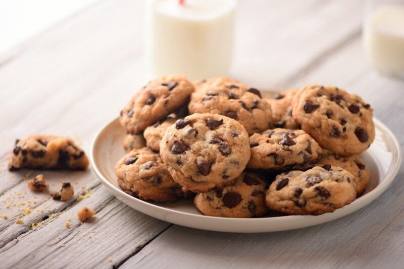 A shallow plate of cookies on a wooden table, next to a glass of milk