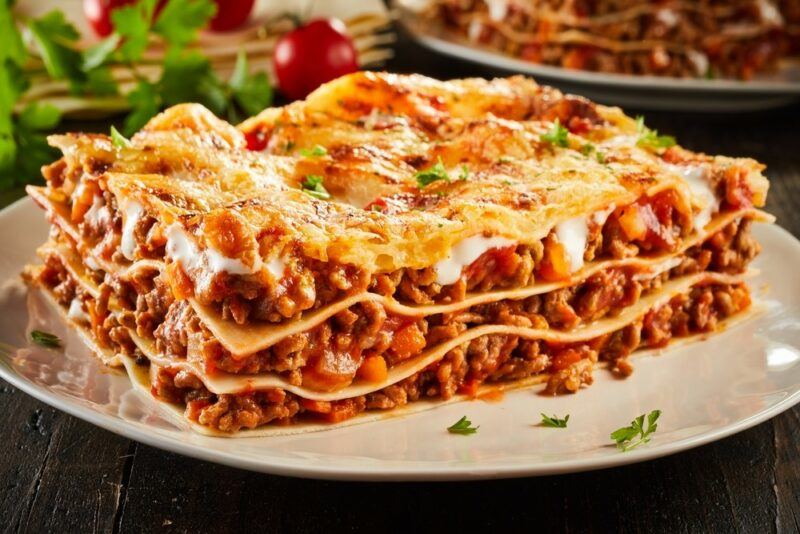 A white plate with a large piece of Italian lasagna with three layers and a cheesy topping