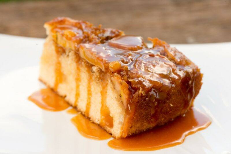 A white plate with a banana and caramel cake that has been drizzled with caramel sauce