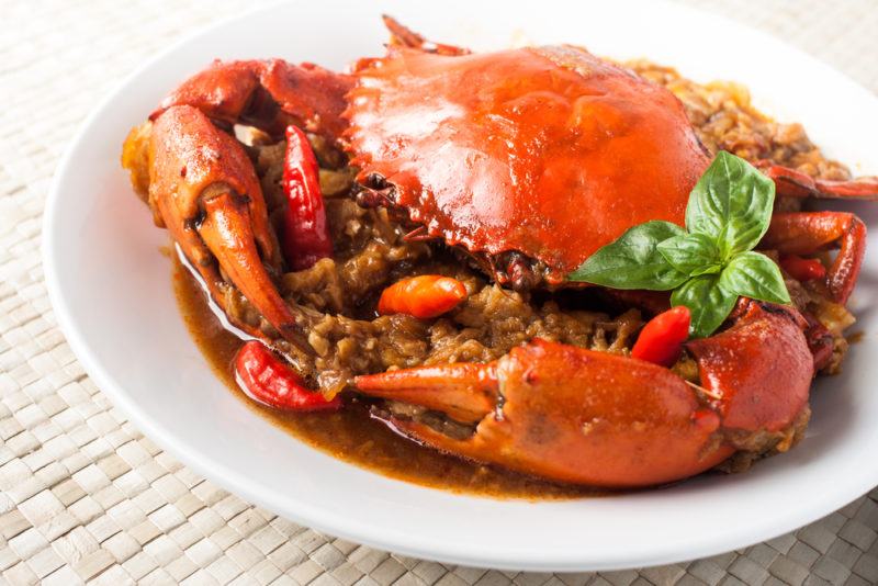 A white plate with a single cooked crab on rice or another type of grain