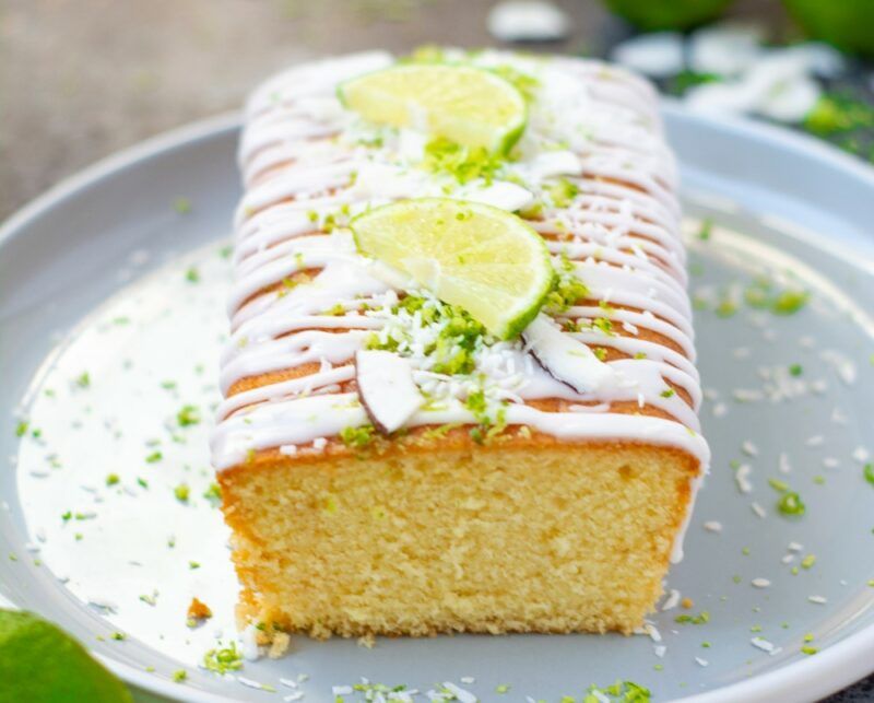 A gray tray with a lime and coconut cake, with white icing and fresh limes on top