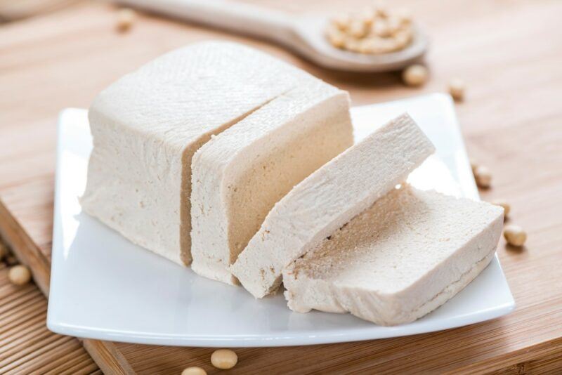 A square white plate with a wedge of tofu and slices of tofu