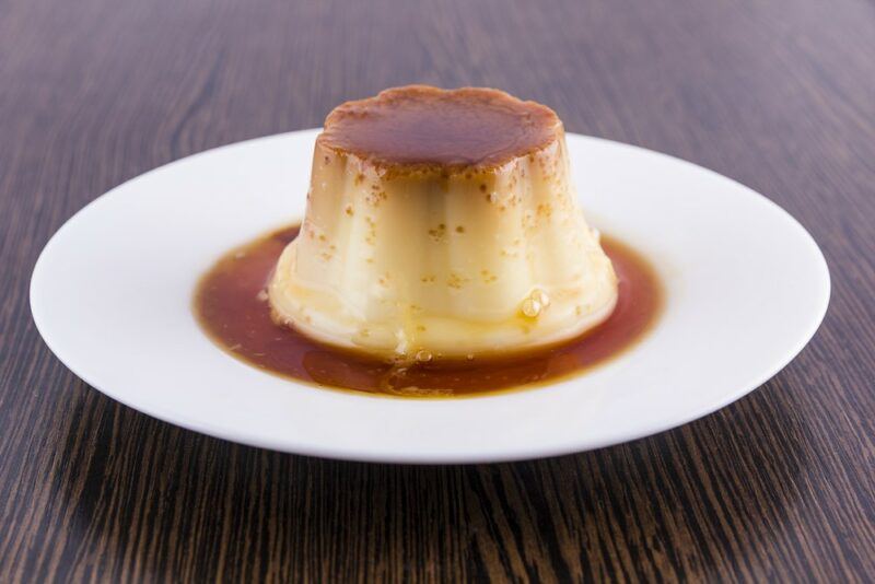 A white plate with a pudding called flan de queso, which is covered in caramel sauce