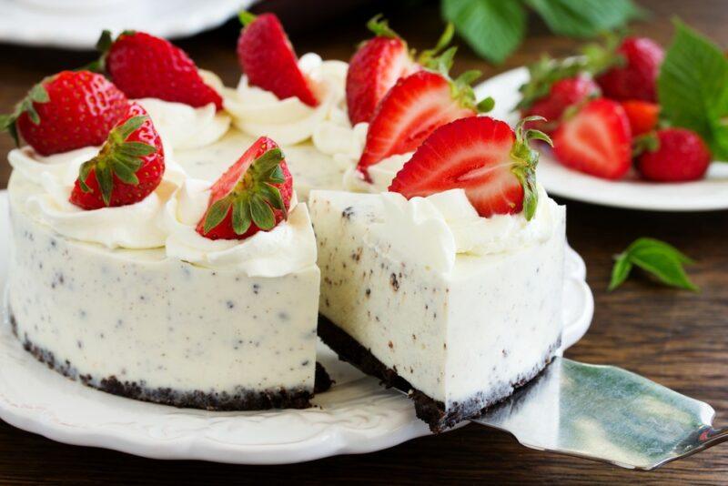 A white plate with a large strawberry and Oreo cake that has been topped with strawberries and cream