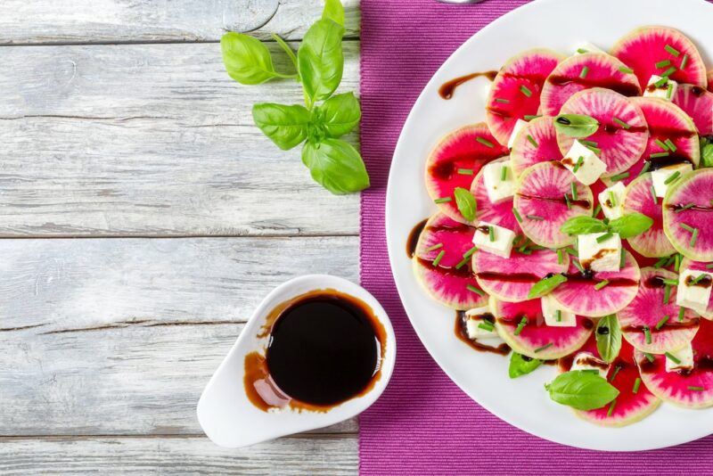 A white dish on a purple piece of cloth containing a watermelon radish salad that has been drizzled with balsamic vinegar