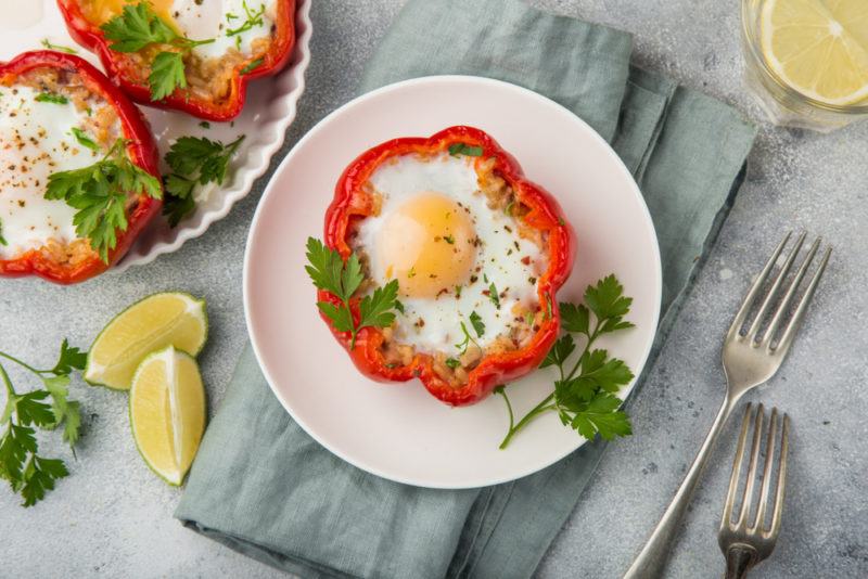 A red pepper ring that contains a cooked egg on a white plate, with another plate nearby that has two more