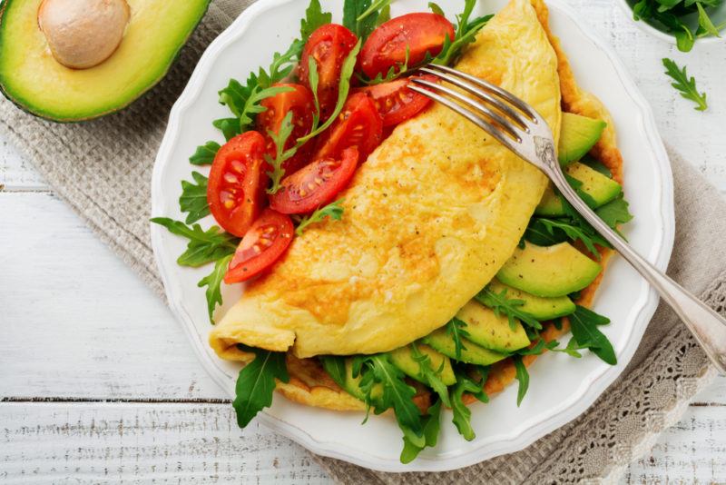 A white plate with a healthy avocado and greens omelet, with tomatoes on the side