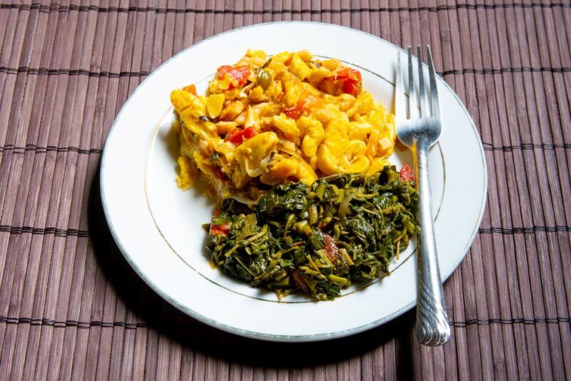 A white plate with callaloo that has been cooked with spices, along with an ackee and codfish dish