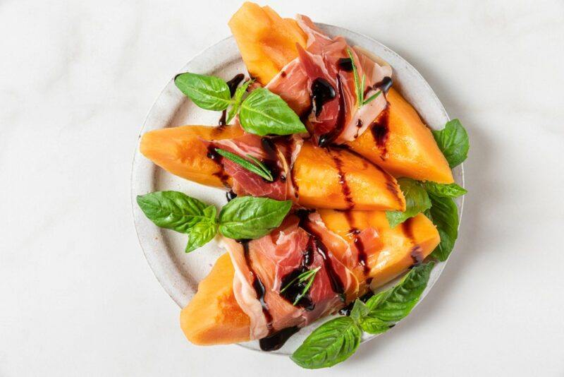 A plate with fresh cantaloupe , balsamic vinegar, and ham