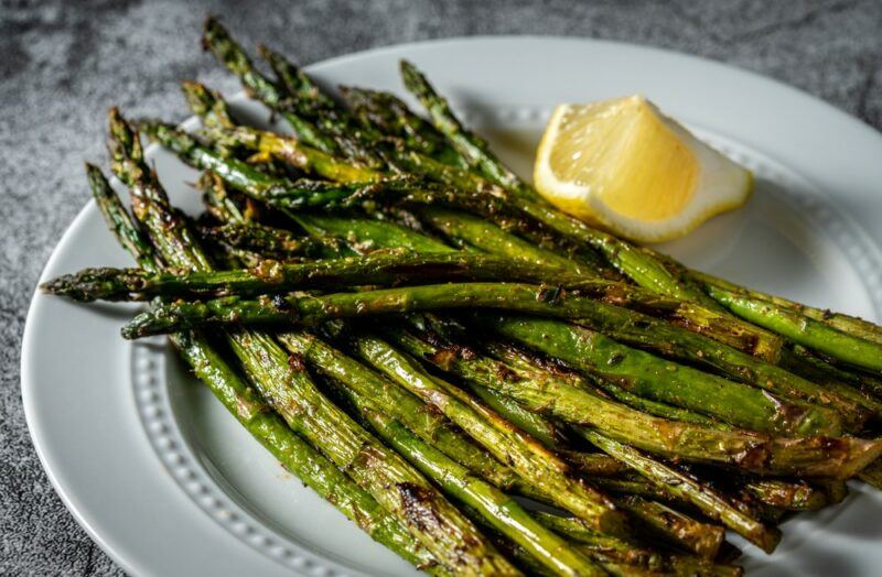 A white plate with many spears of cooked asparagus, plus a lemon wedge