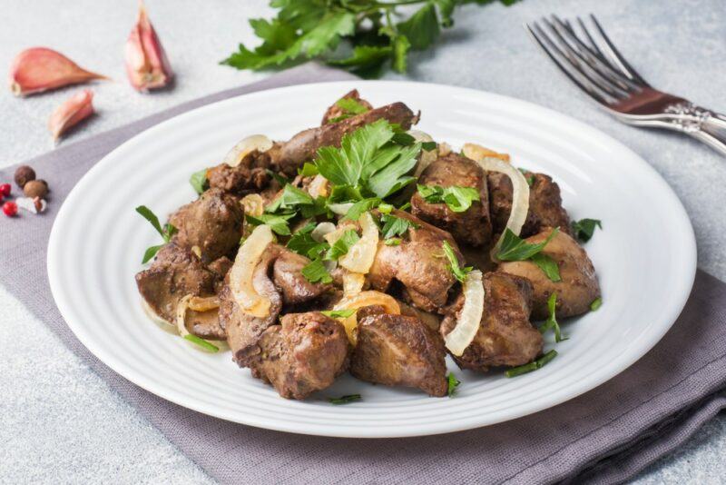 A white dish with cooked chicken liver and onions, next to a fork