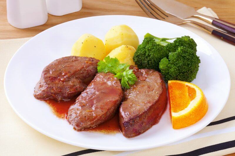 A white plate with cooked pieces of liver, potatoes, and vegetables