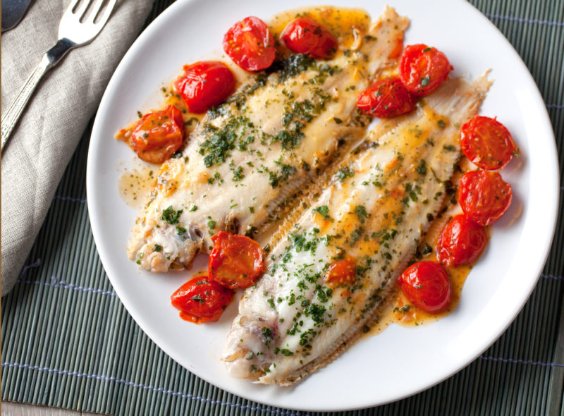 A white plate with two pieces of cooked sole and cooked cherry tomatoes