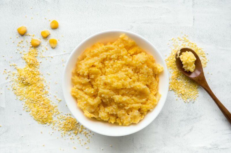 A white dish that contains cornmeal porridge next to a spoon