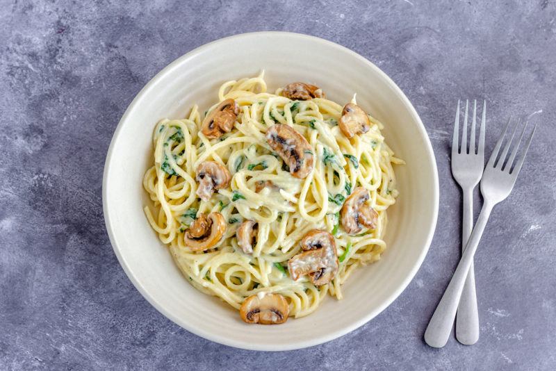 A white plate that contains a creamy mushroom pasta next to two forks