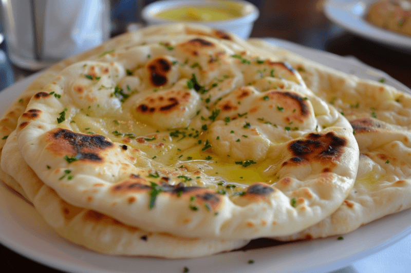 A large white plate with a few pieces of homemade pita bread or naan bread.